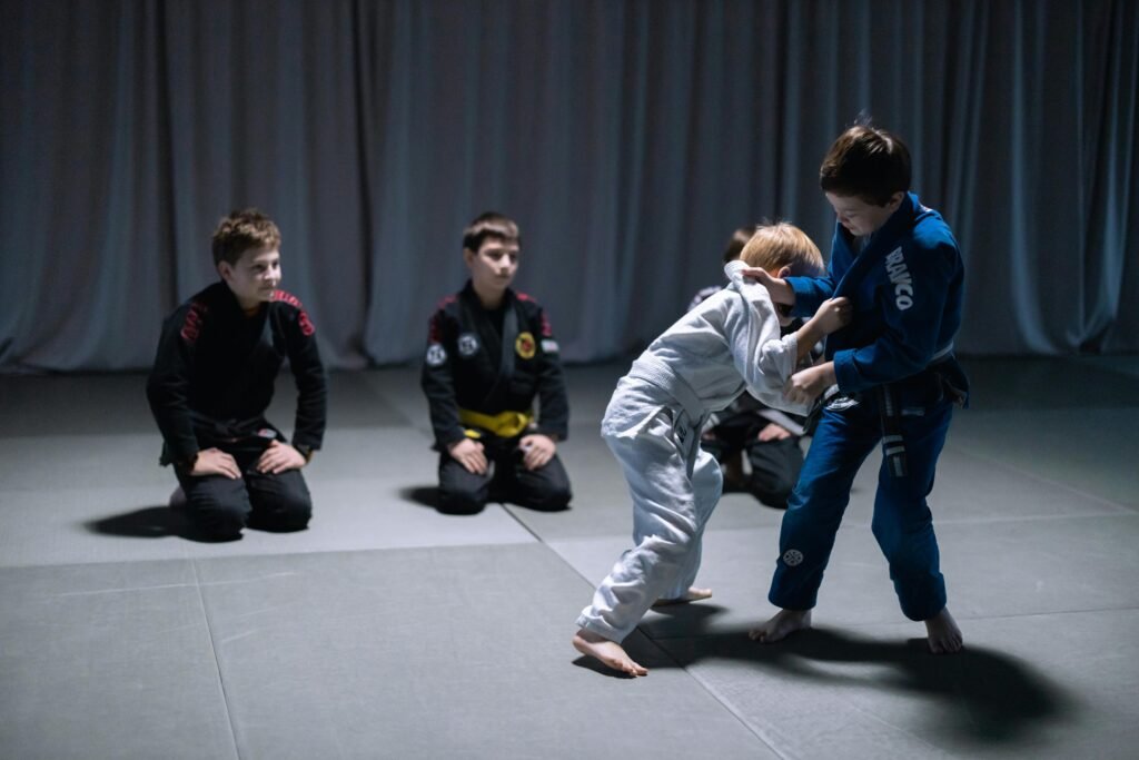 Children practicing jiu jitsu in a gym setting, wearing gi uniforms, during sparring session.